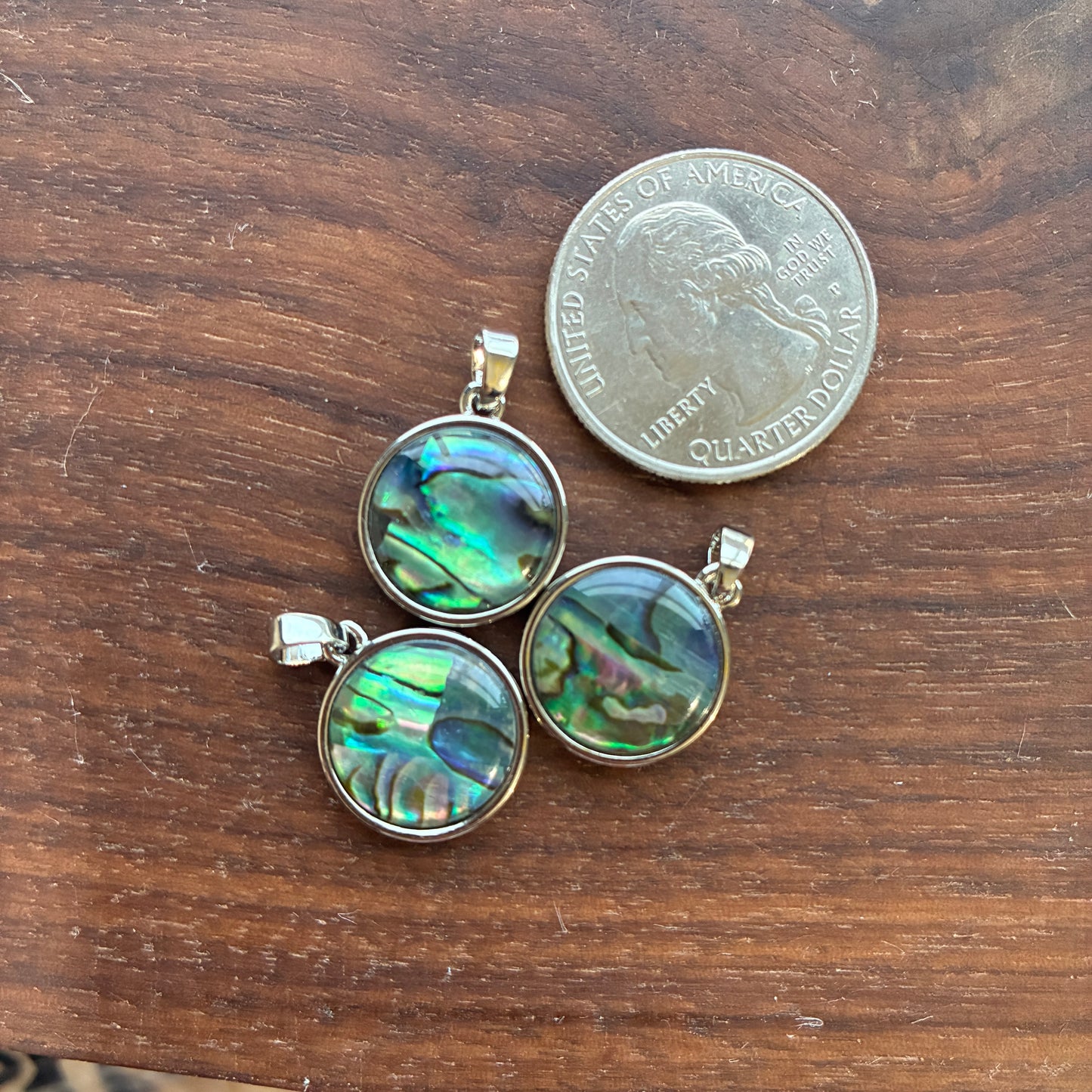 Three abalone shell pendants on a wooden surface with a quarter for scale.