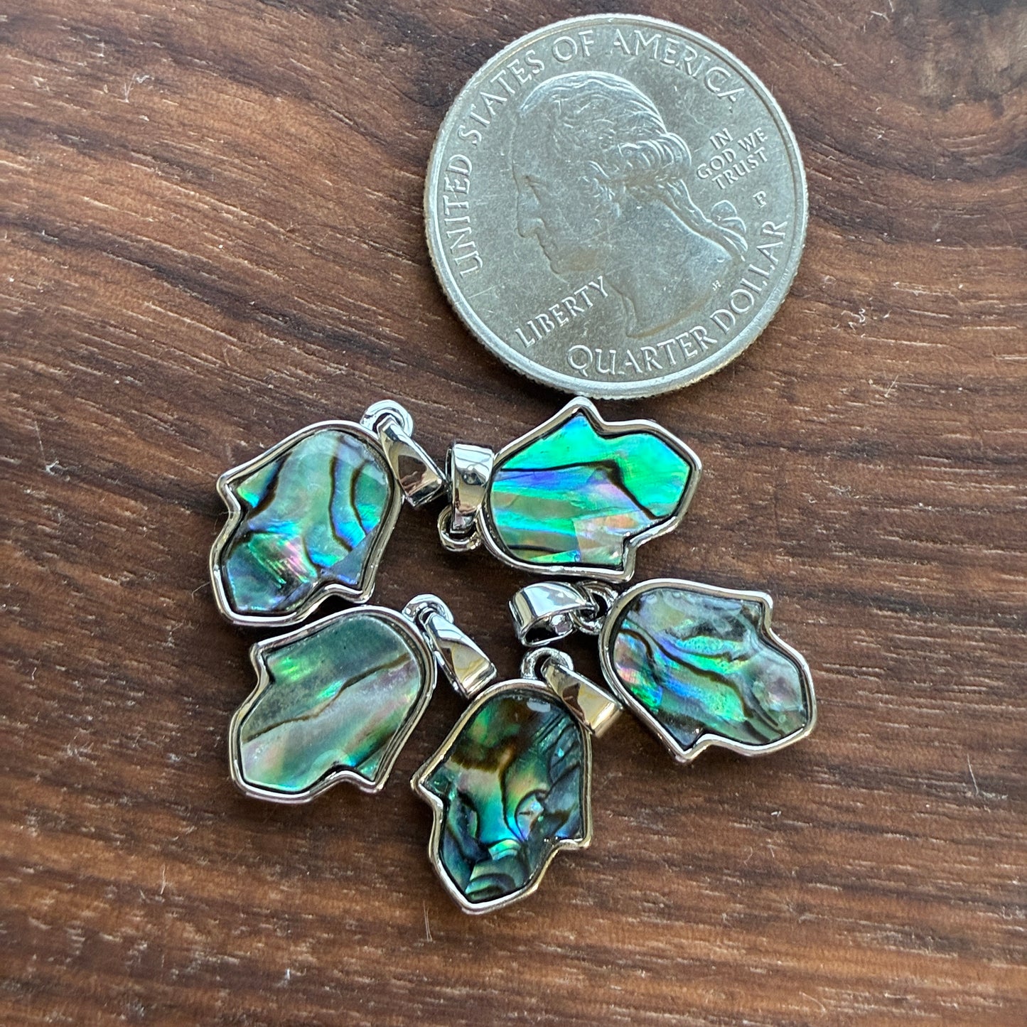 Four abalone shell pendants on a wooden surface with a quarter for scale.