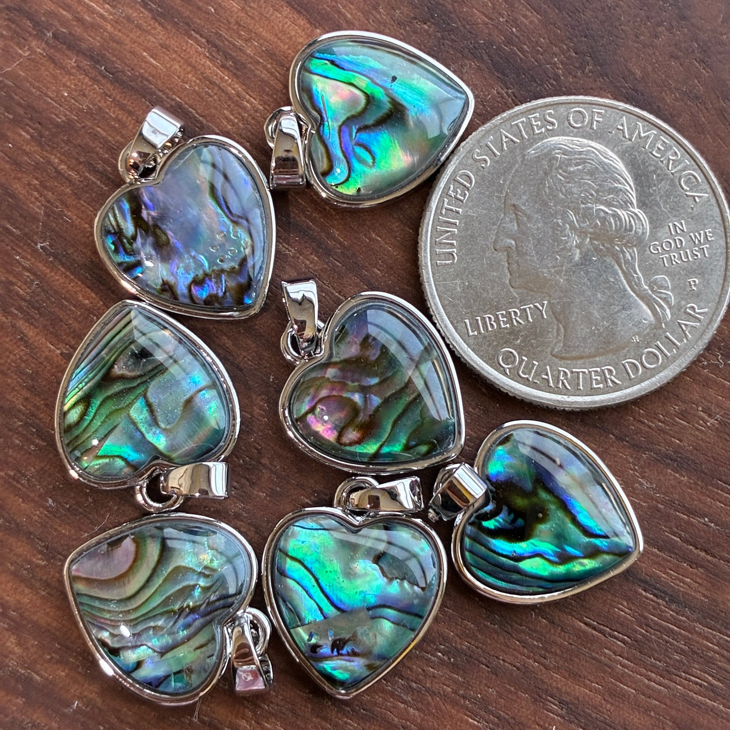 Heart-shaped abalone shell pendants on a wooden surface with a quarter for scale.