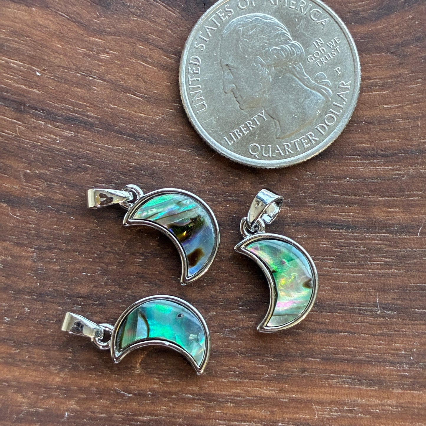 Three moon-shaped pendants on a wooden surface with a quarter for scale.