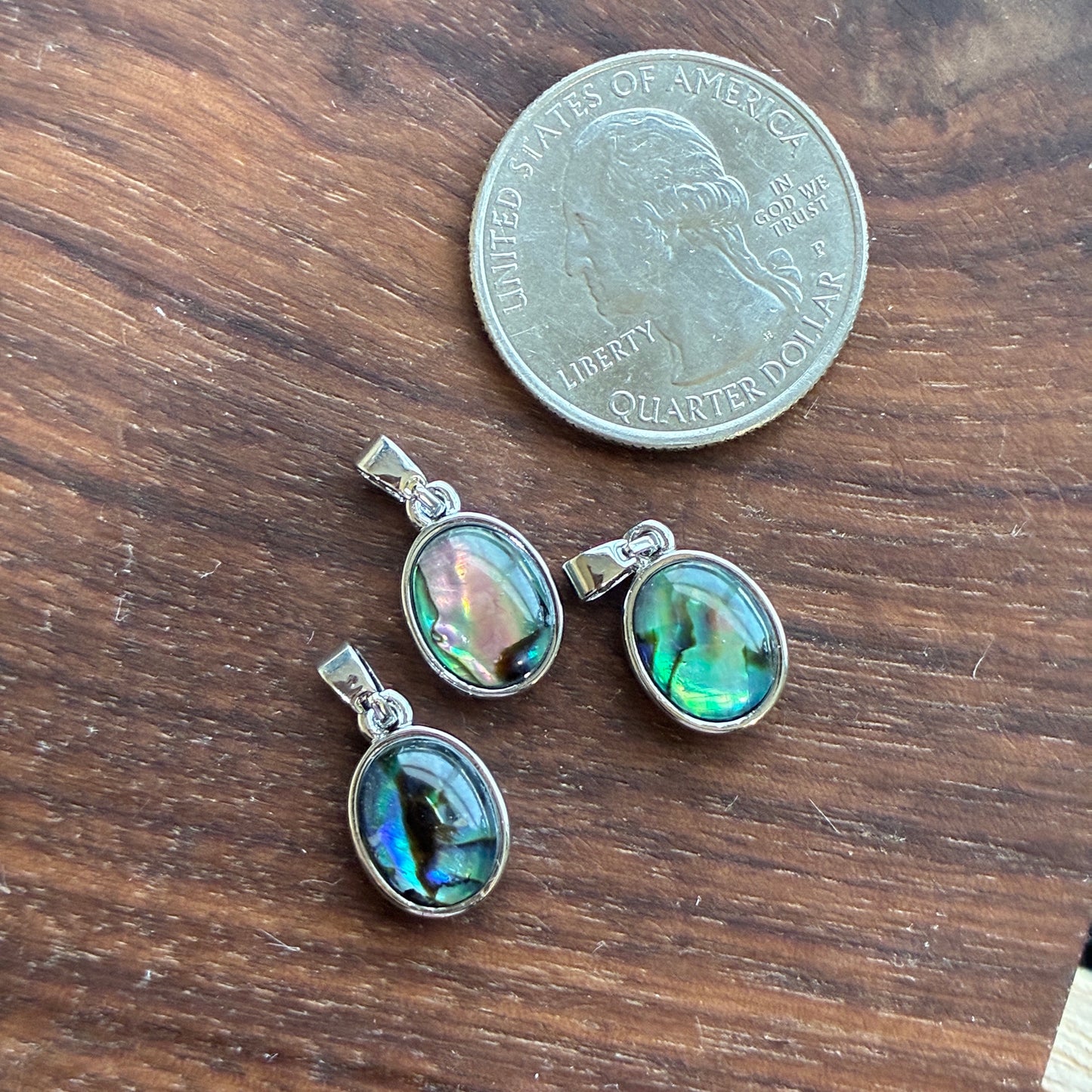 Three abalone shell pendants on a wooden surface with a quarter for scale.