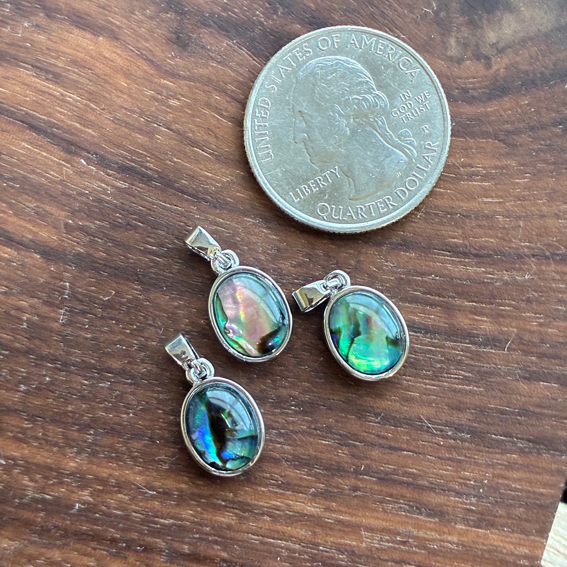 Three abalone shell pendants on a wooden surface with a quarter for scale.