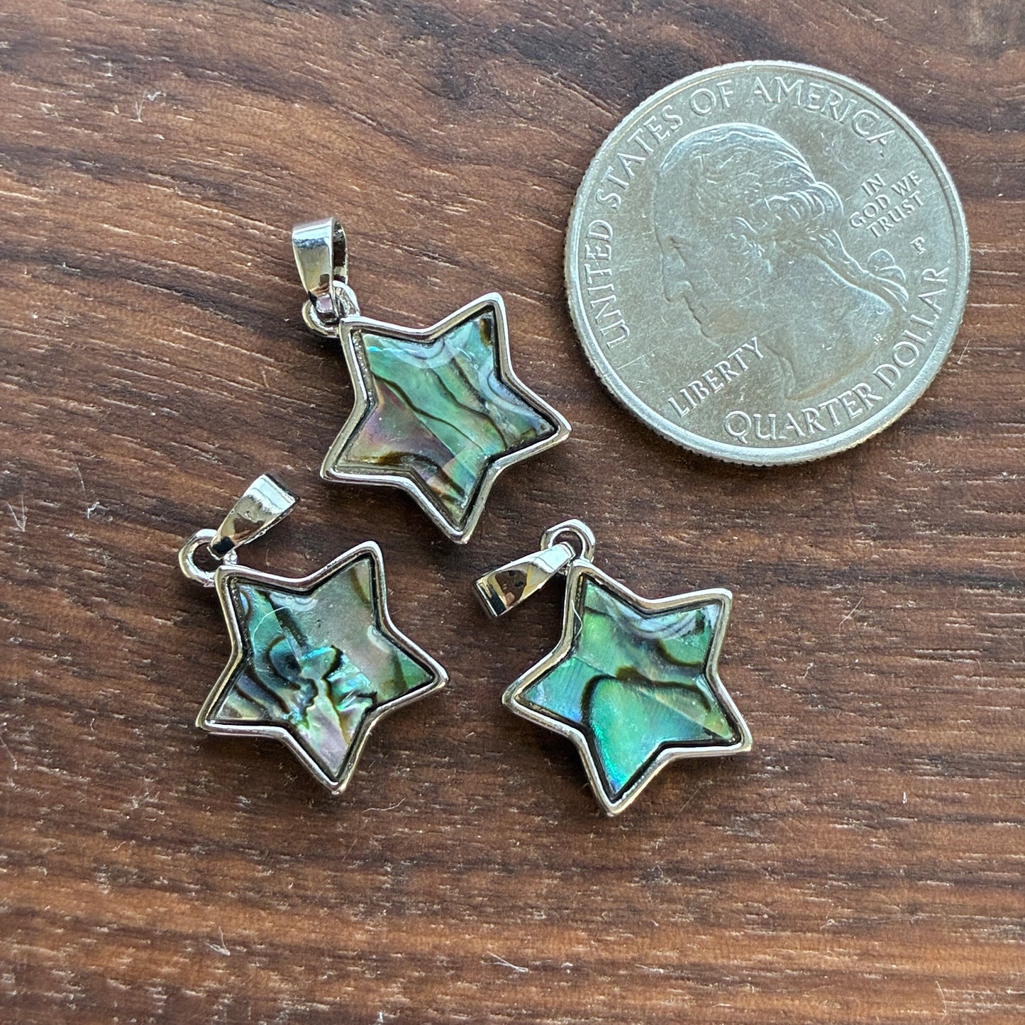 Three star-shaped Abalone pendants with green iridescent center on a wooden surface next to a quarter.