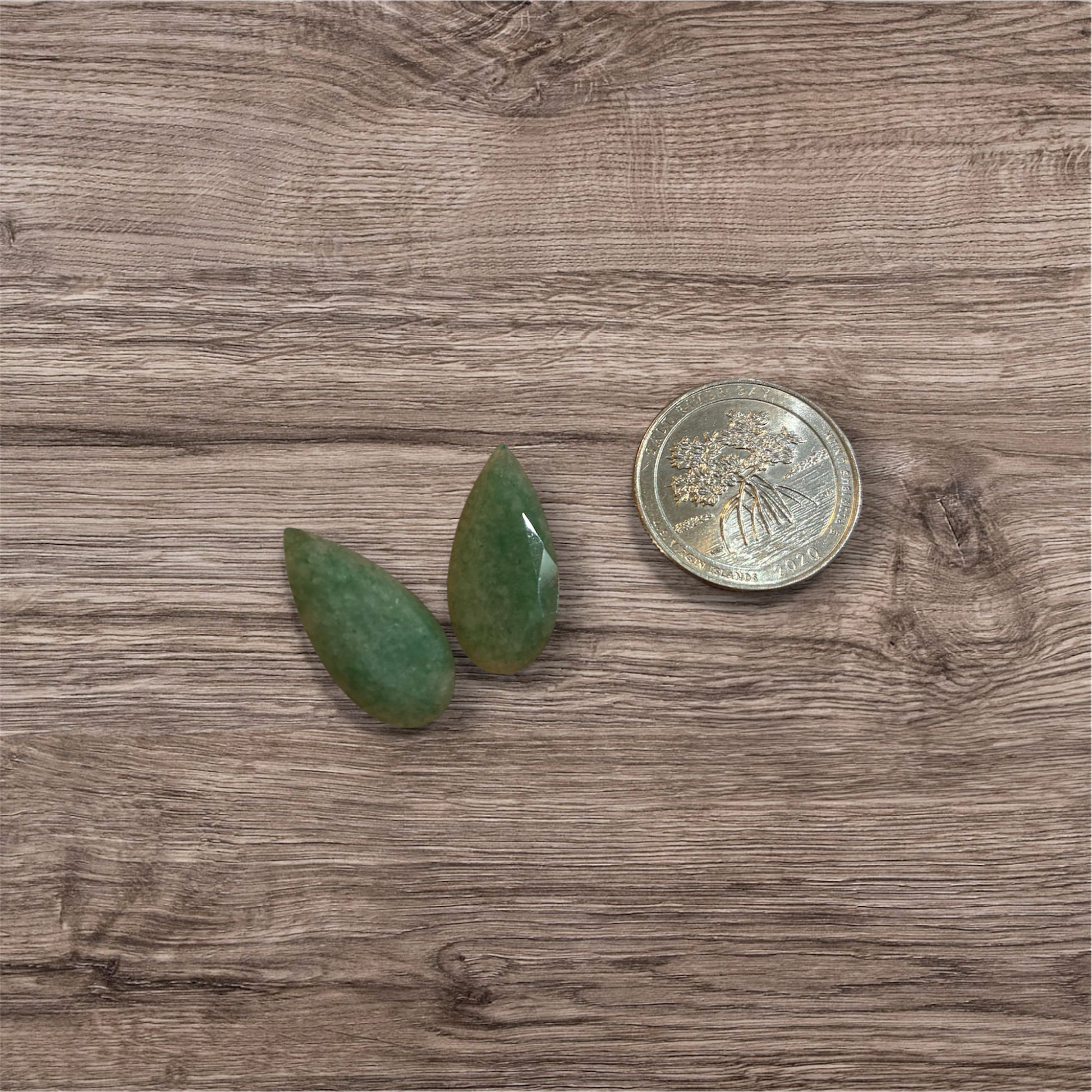 Two green stones on a wooden surface next to a coin for scale.