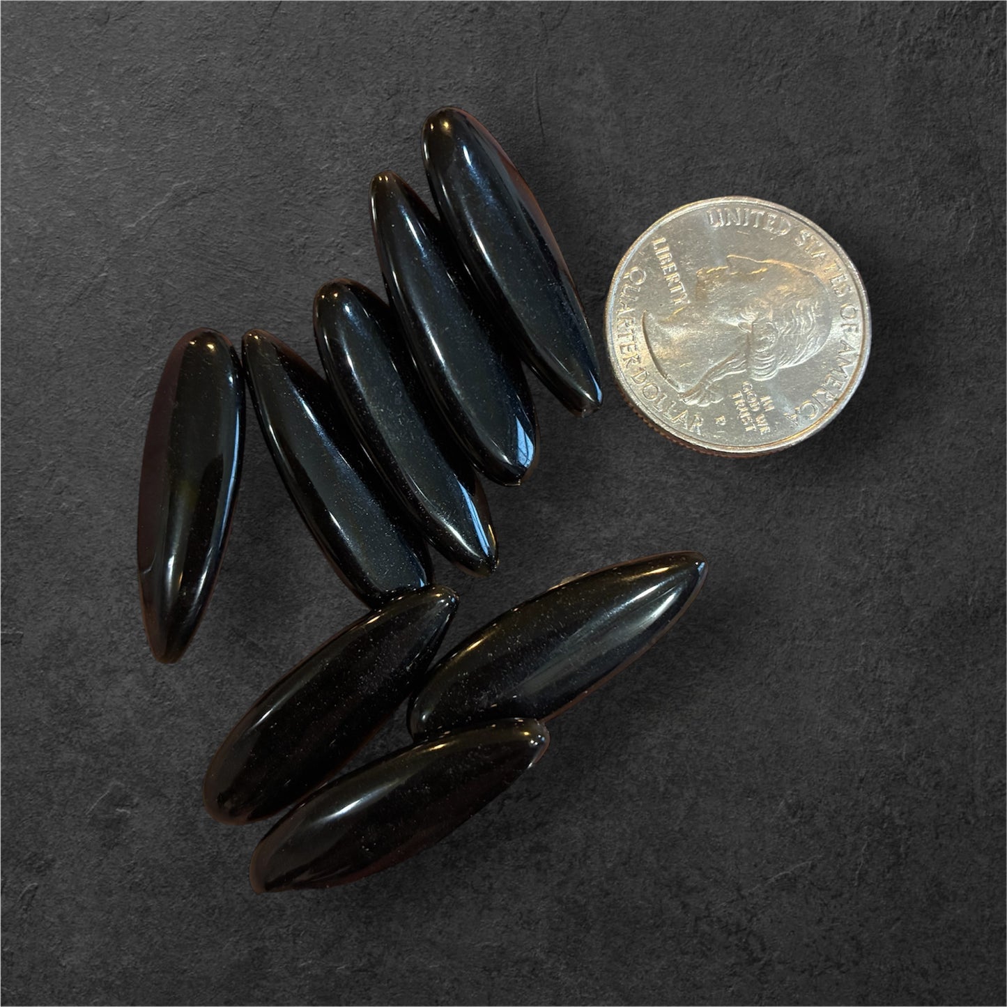 Black Obsidian oval beads on a dark surface with a coin for scale