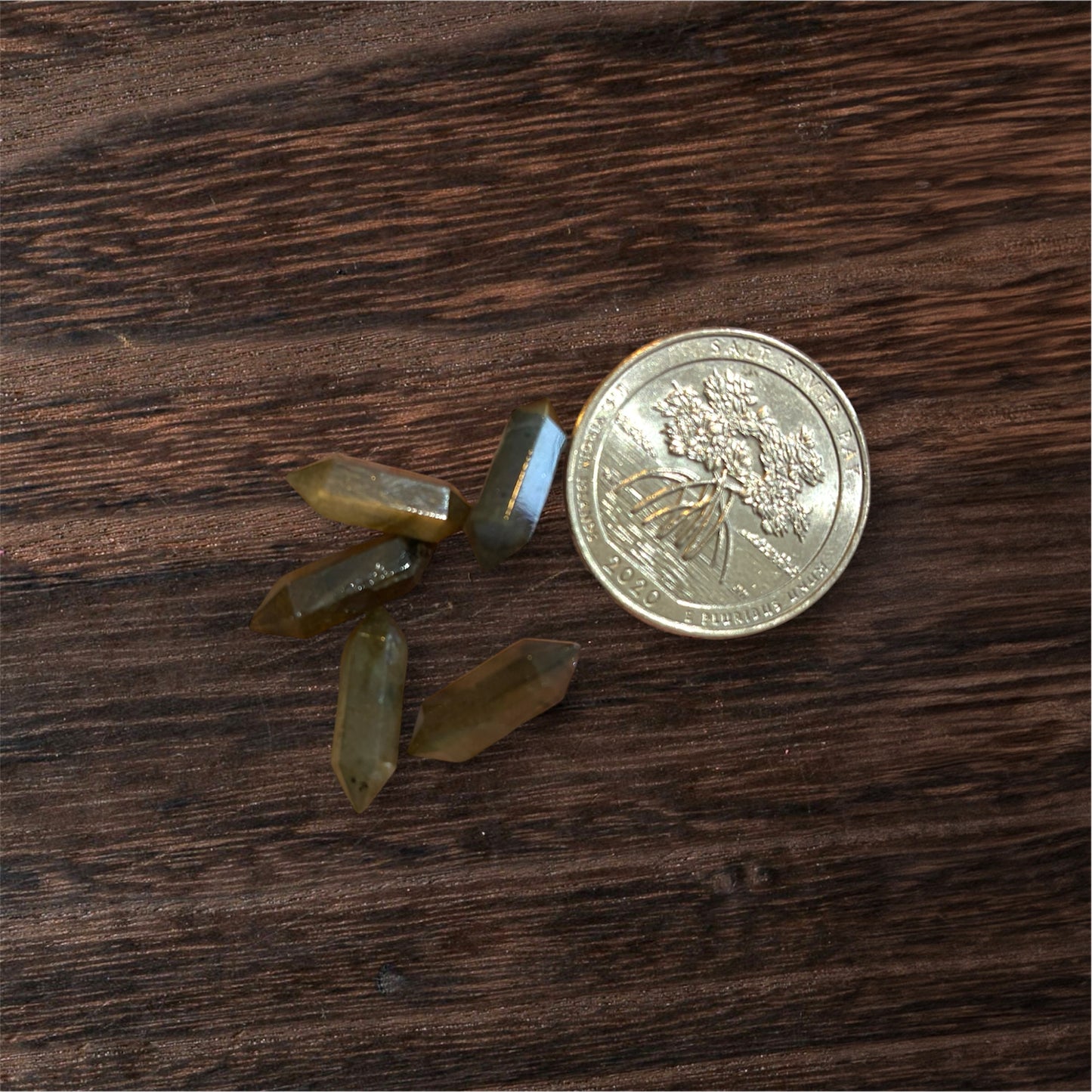 Small crystal points next to a coin on a wooden surface