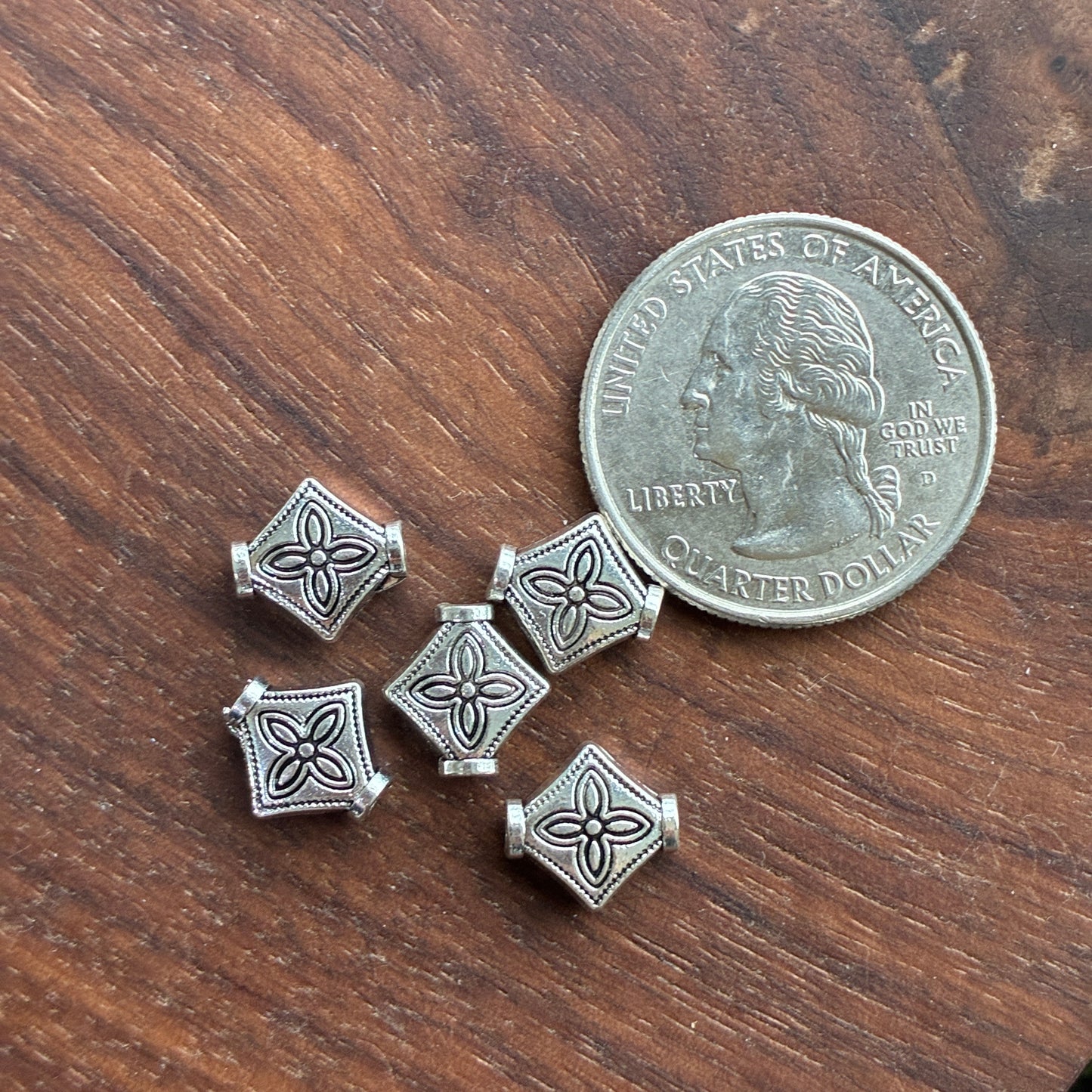 Four silver square-shaped charms on a wooden surface with a quarter for scale.