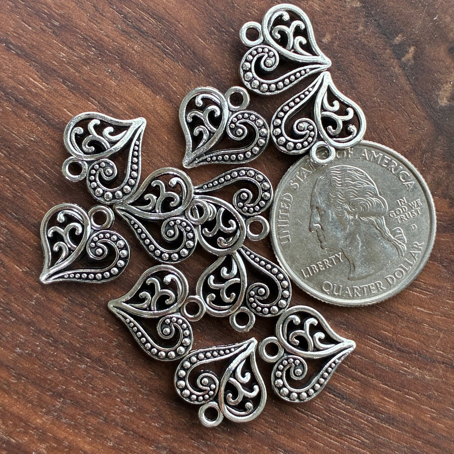 Silver Heart pendants on a wooden surface with a quarter for scale.