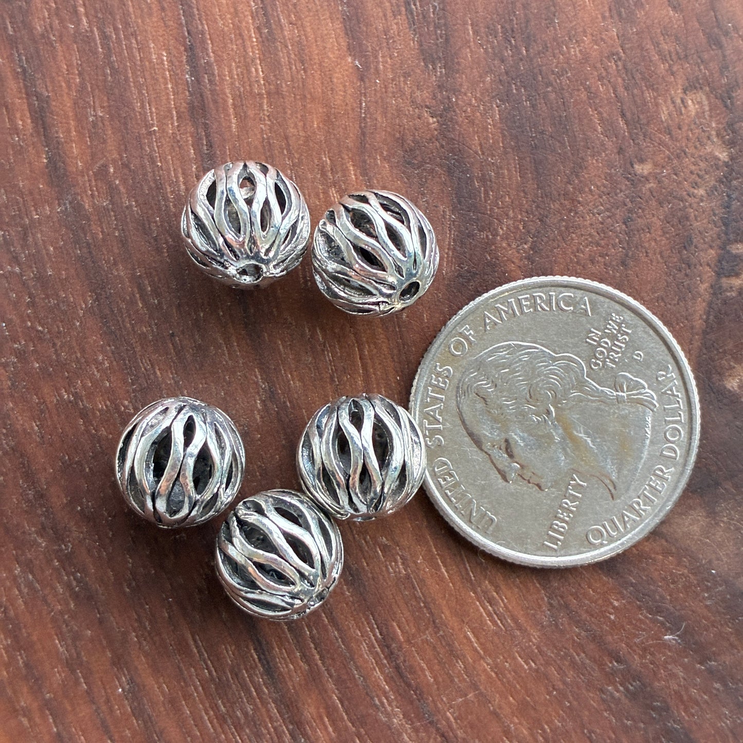 Silver beads on a wooden surface with a quarter for scale