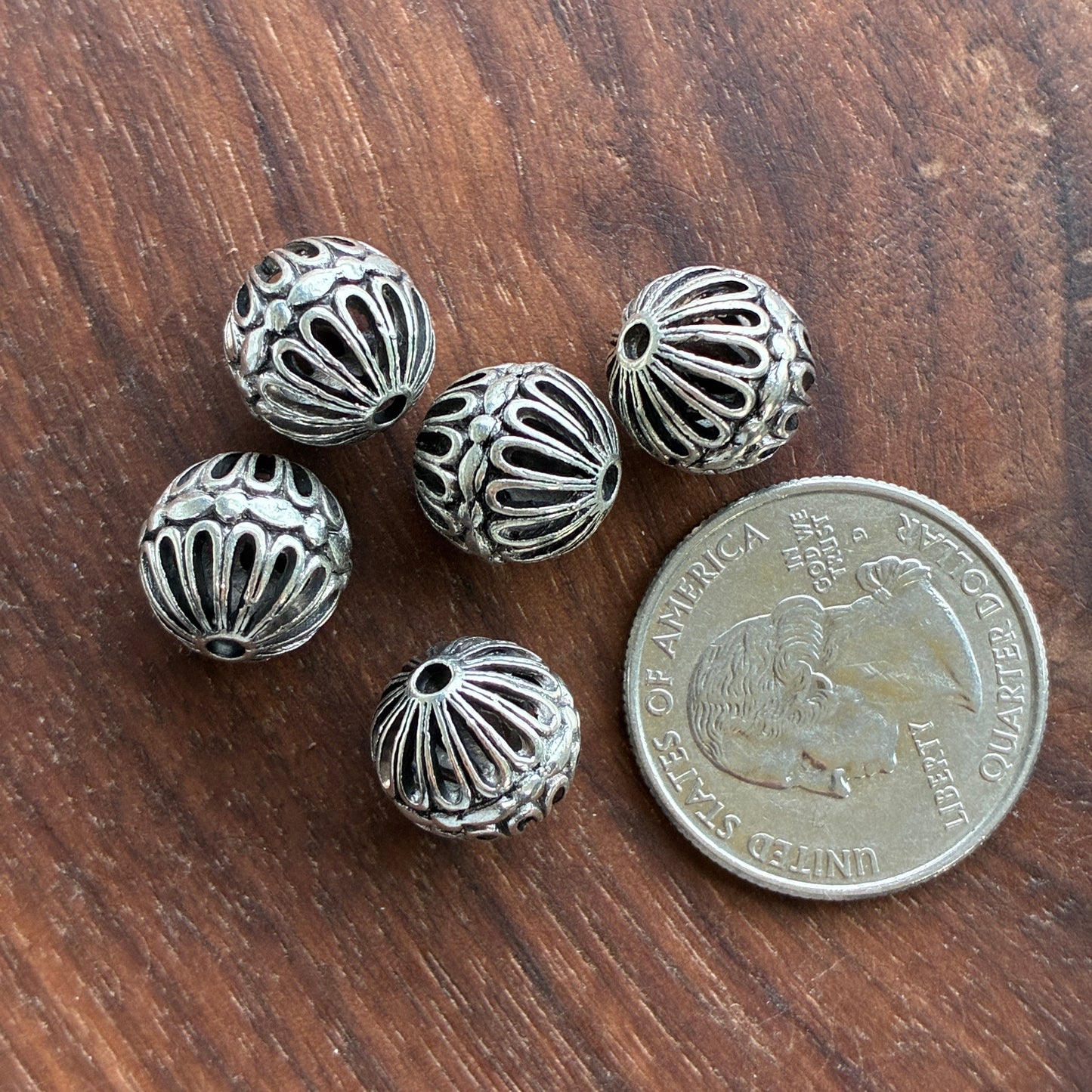 Silver beads on a wooden surface with a quarter for scale