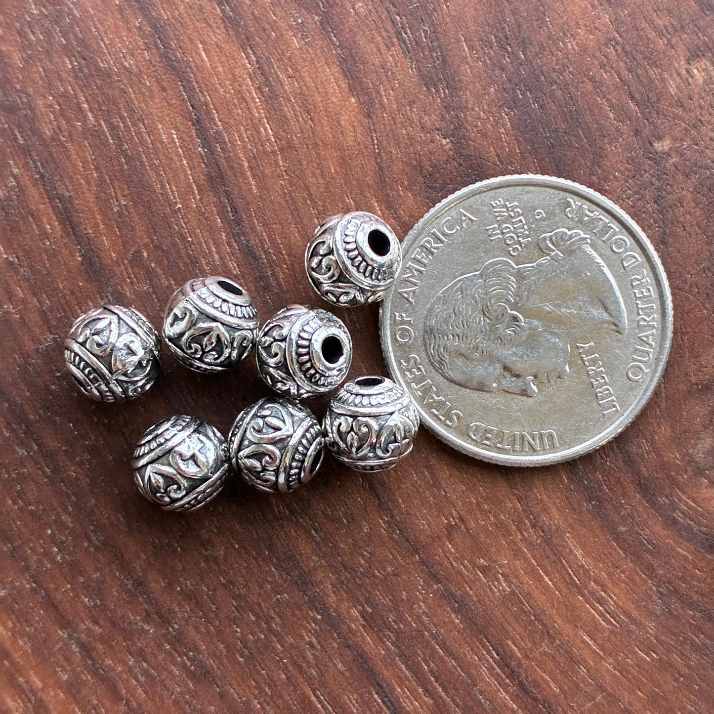 Silver beads on a wooden surface with a quarter for scale