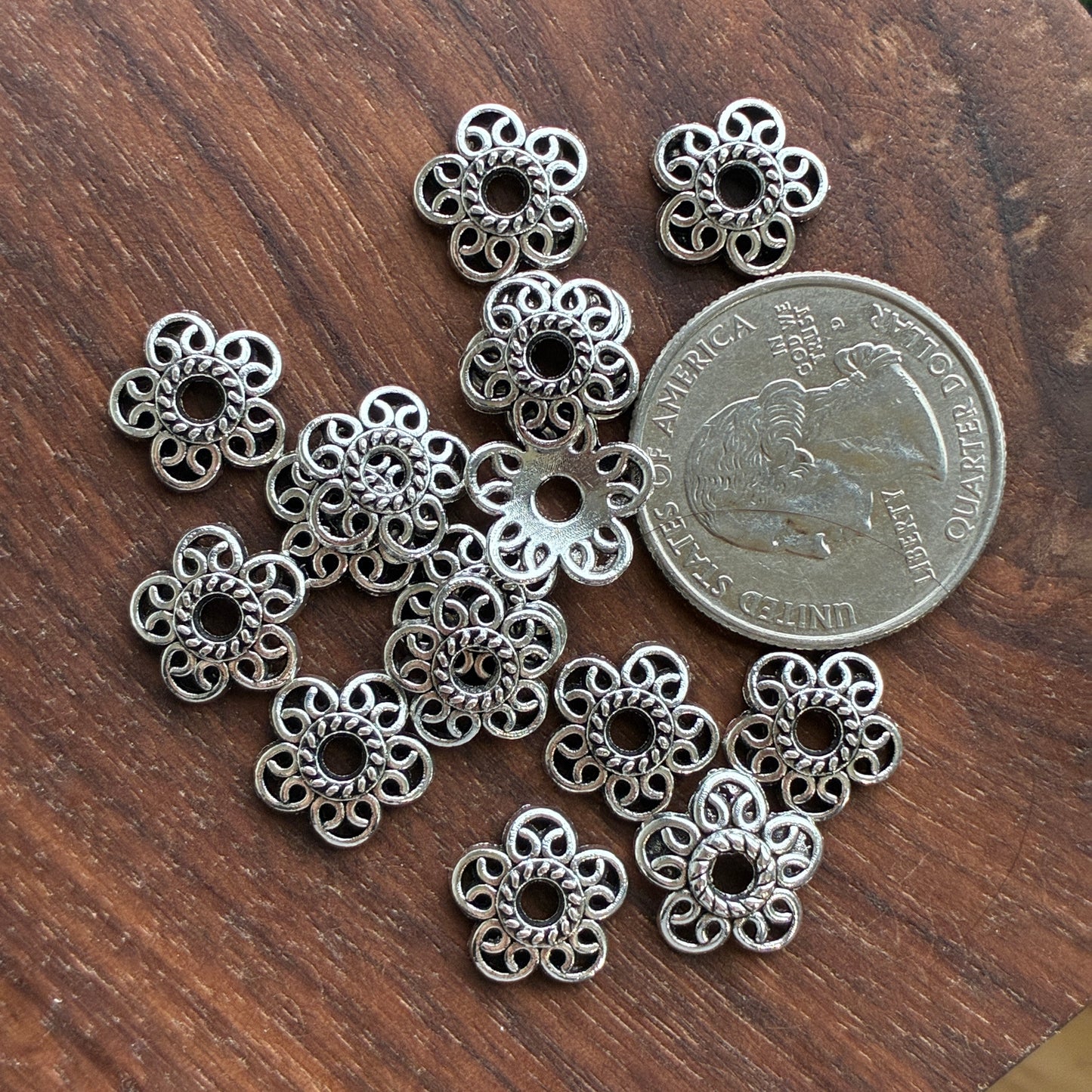 Silver floral metal bead cap on a wooden surface with a quarter for scale.