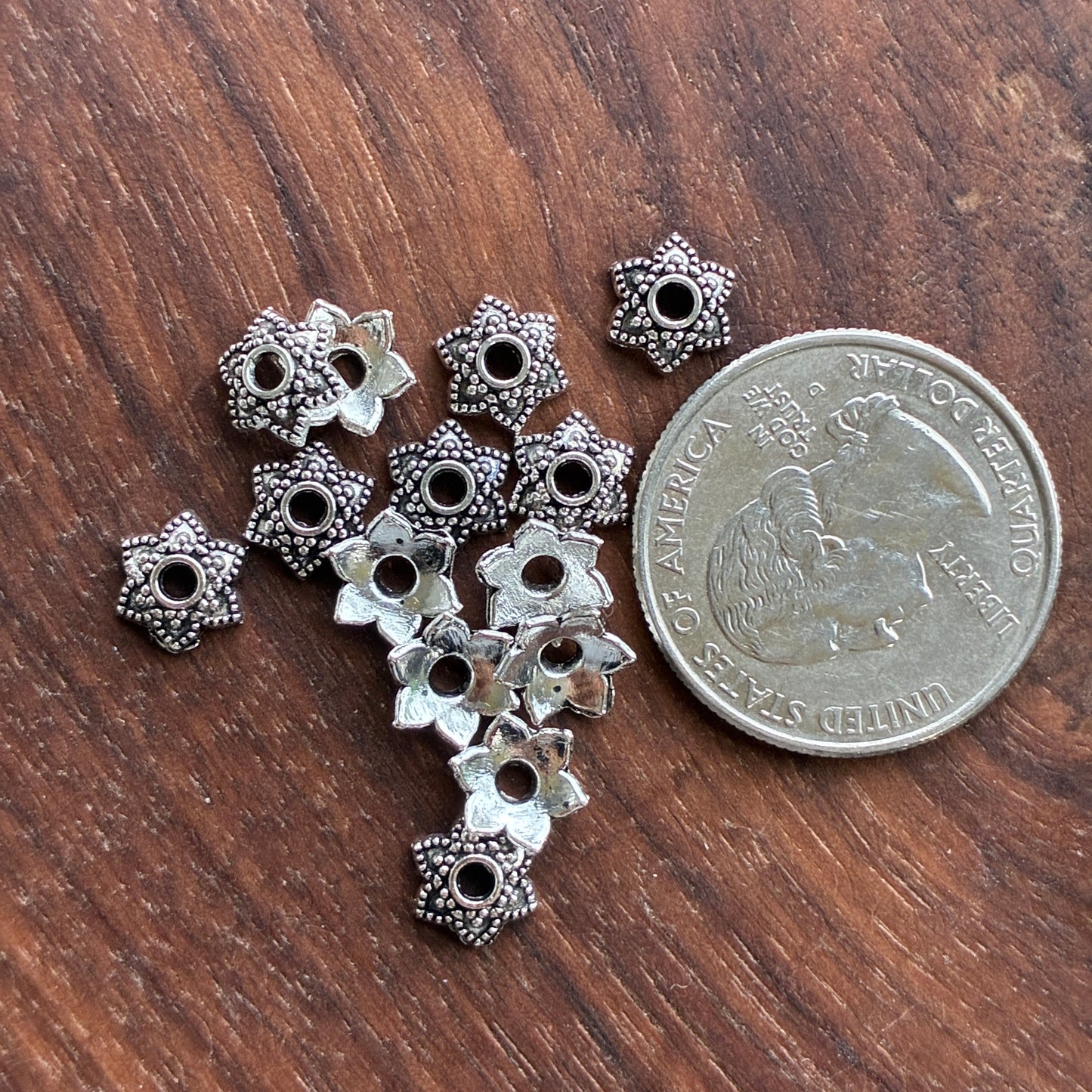 Silver floral bead cap on a wooden surface with a quarter for scale.