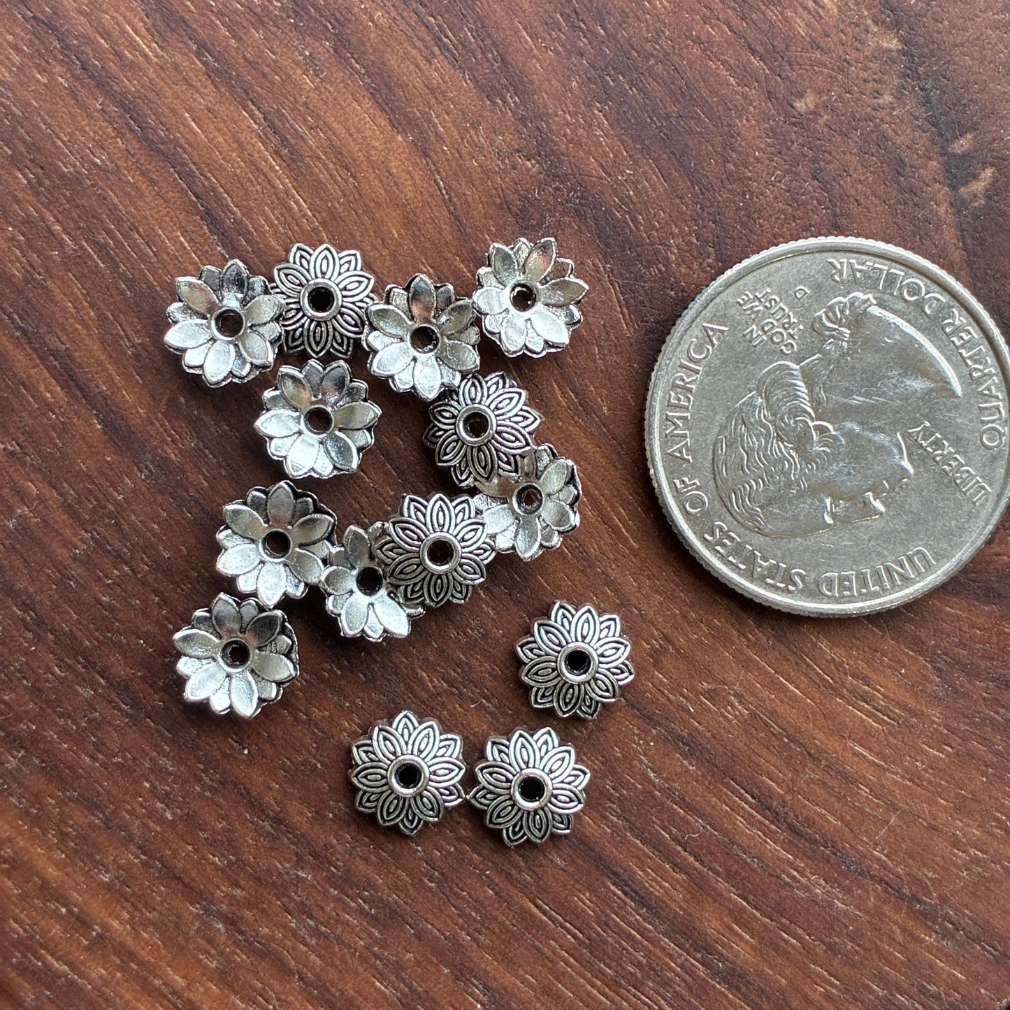 Silver floral bead cap on a wooden surface with a quarter for scale.