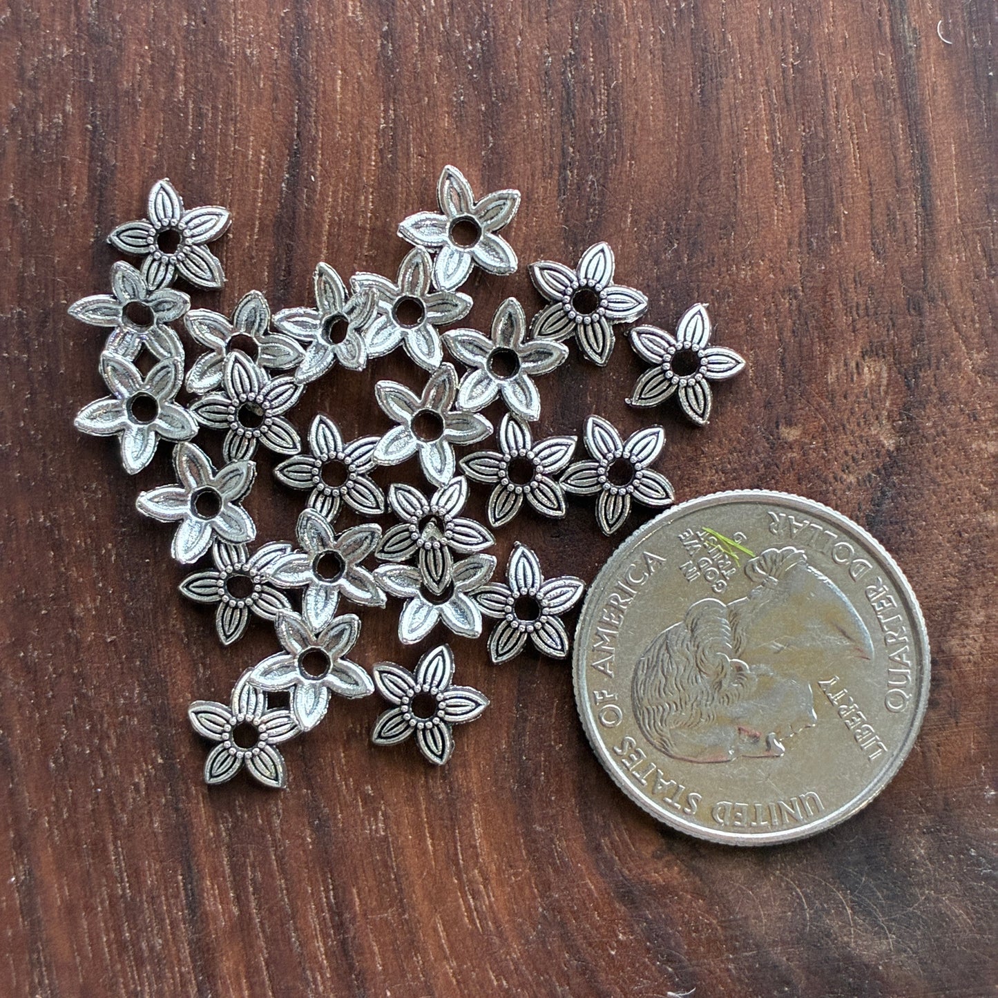 Silver flower-shaped beads next to a coin on a wooden surface