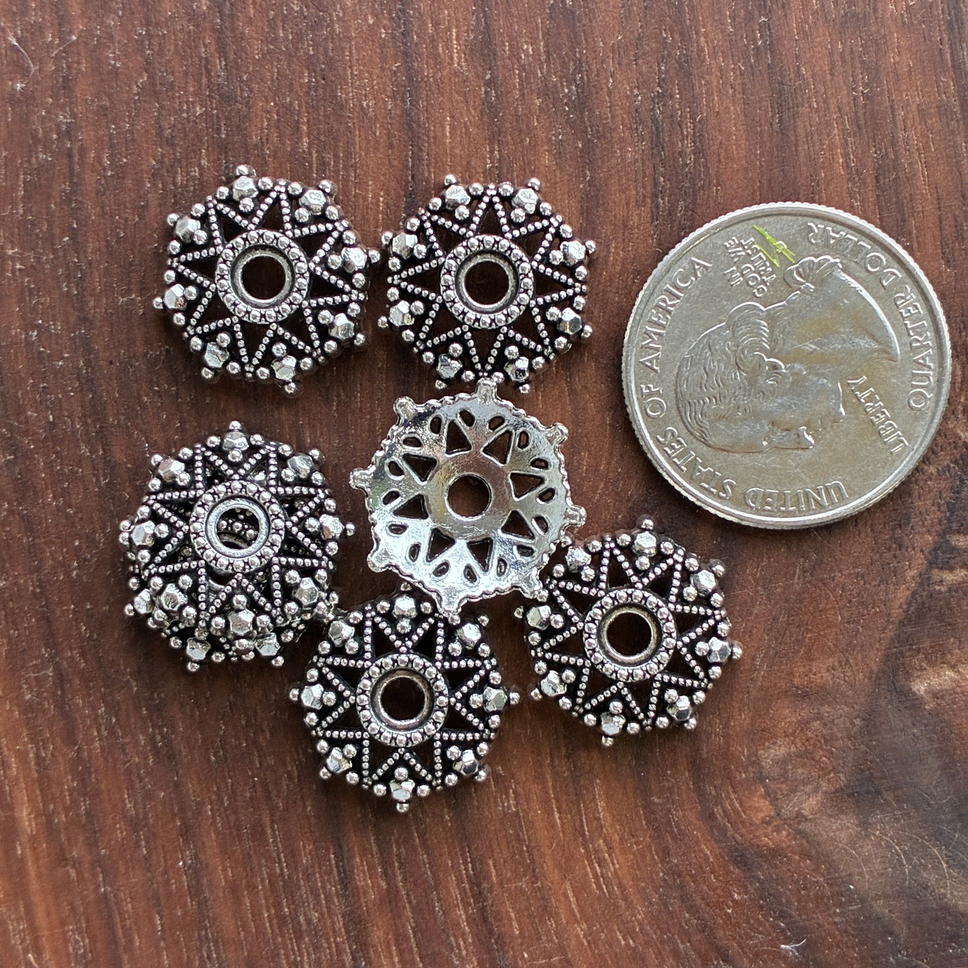 Silver decorative beads on a wooden surface with a quarter for scale.