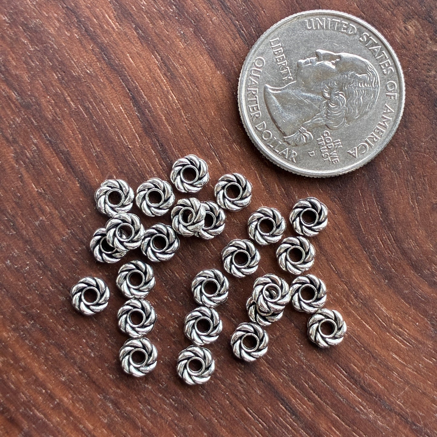 Silver spacers on a wooden surface with a quarter for scale