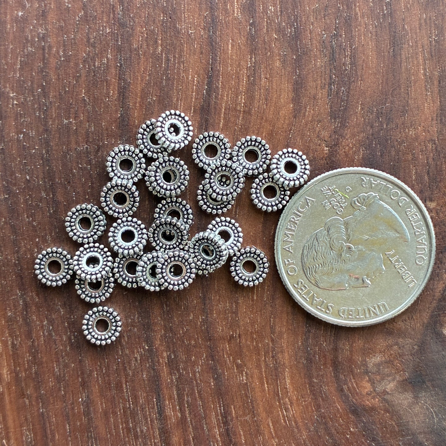 Silver beaded jewelry components next to a quarter on a wooden surface