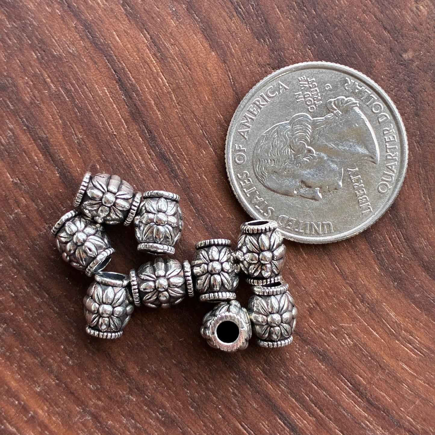 Silver beads with intricate designs on a wooden surface next to a quarter.
