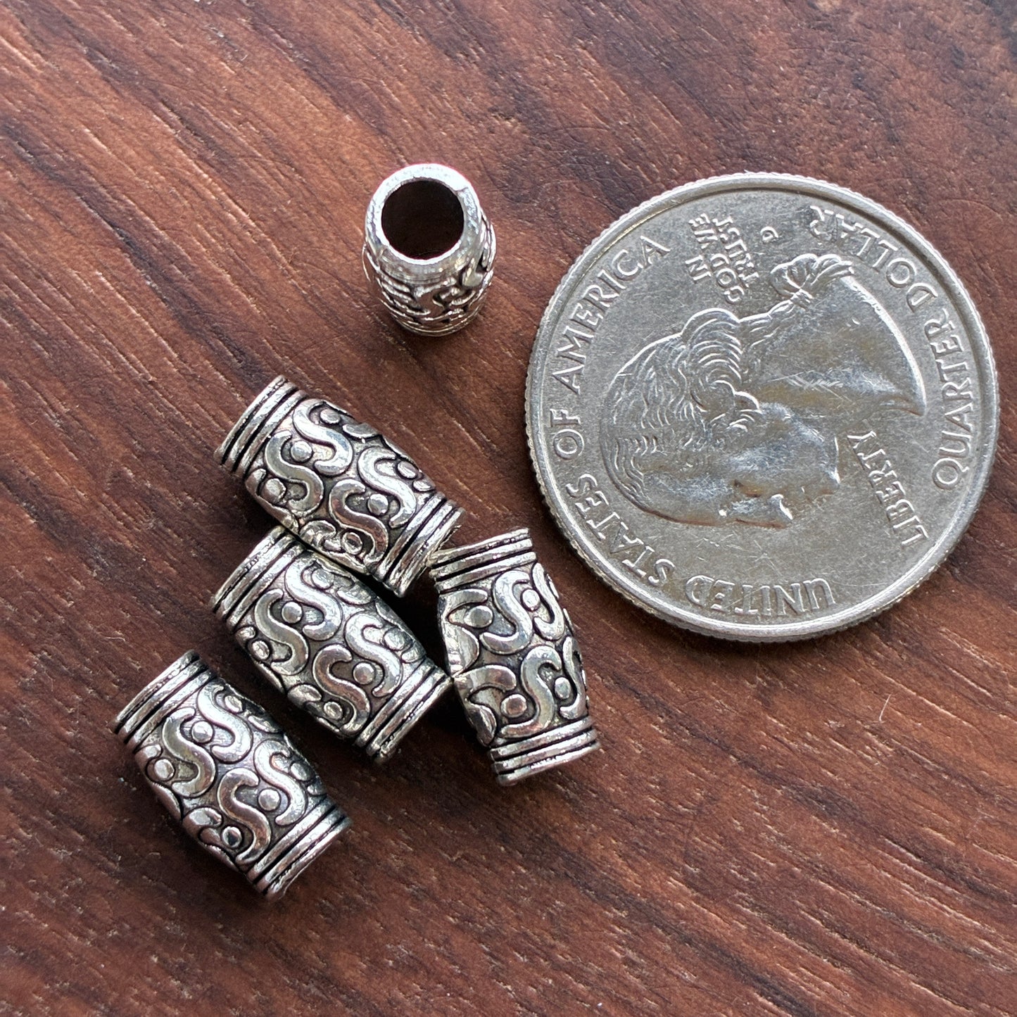 Silver cylindrical beads on a wooden surface with a quarter for scale.
